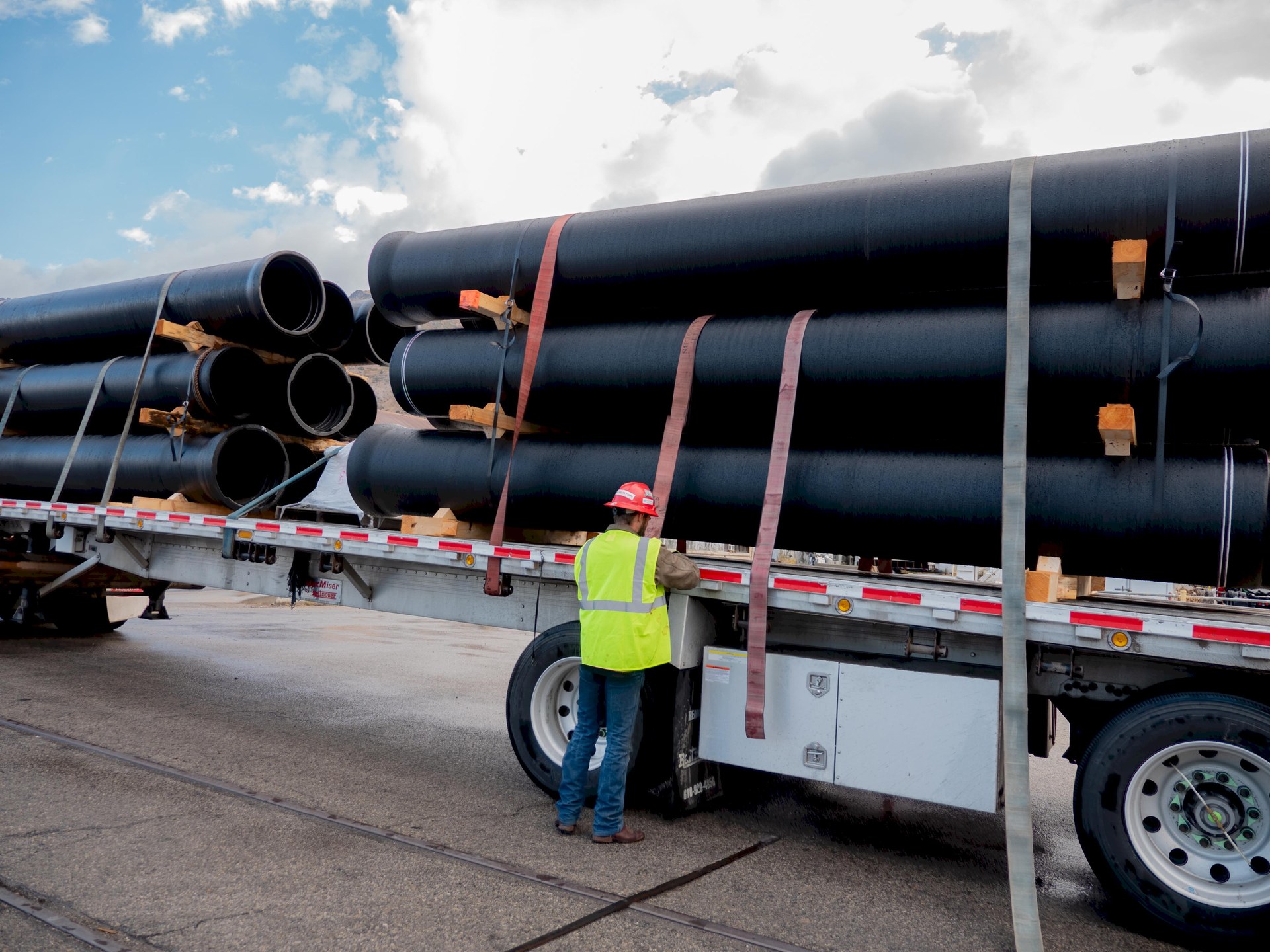 Worker checking strapped pipe bundles on a flatbed trailer
