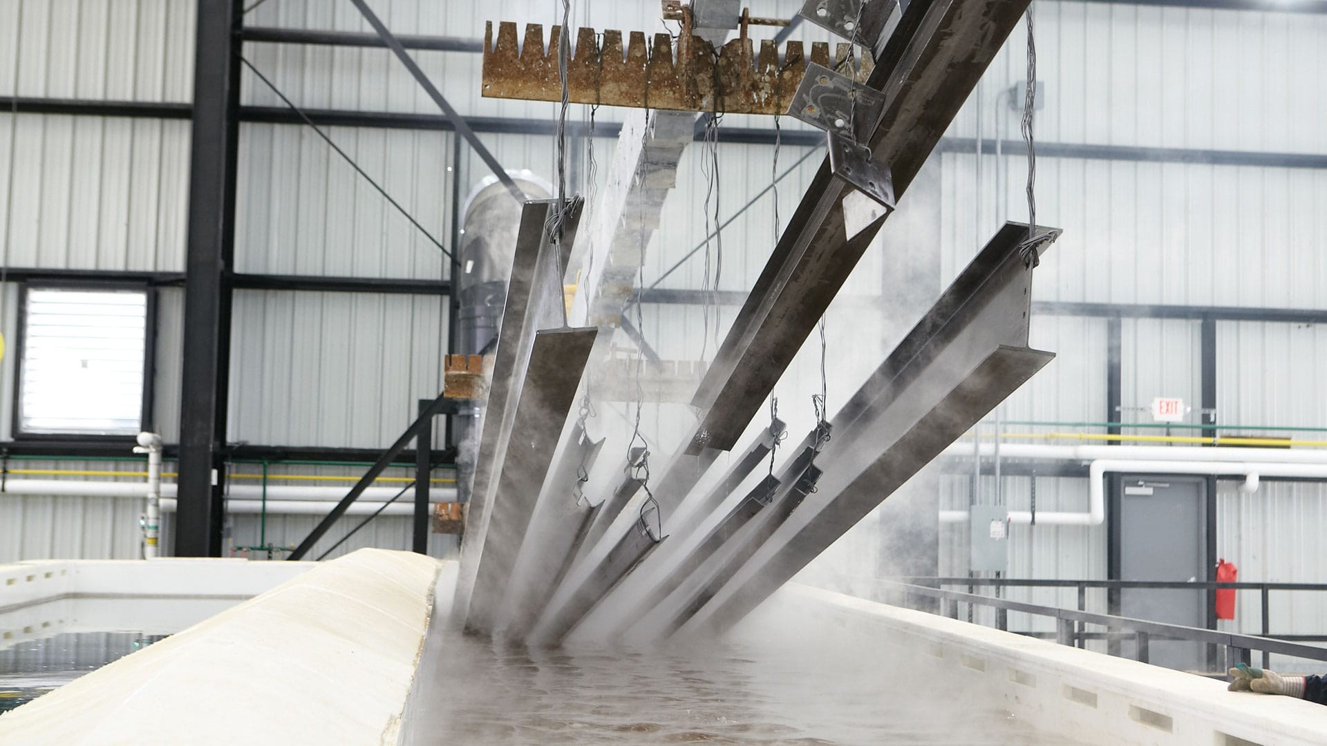 Steel sections being dipped into molten zinc kettle during hot-dip galvanizing